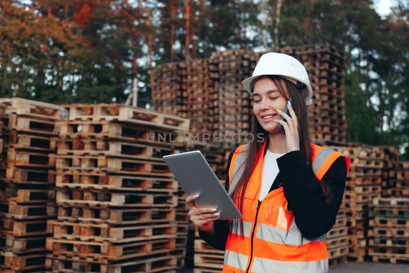 Woman order picker speaking on phone with tablet at outdoors warehouse with pallets speak on phone.