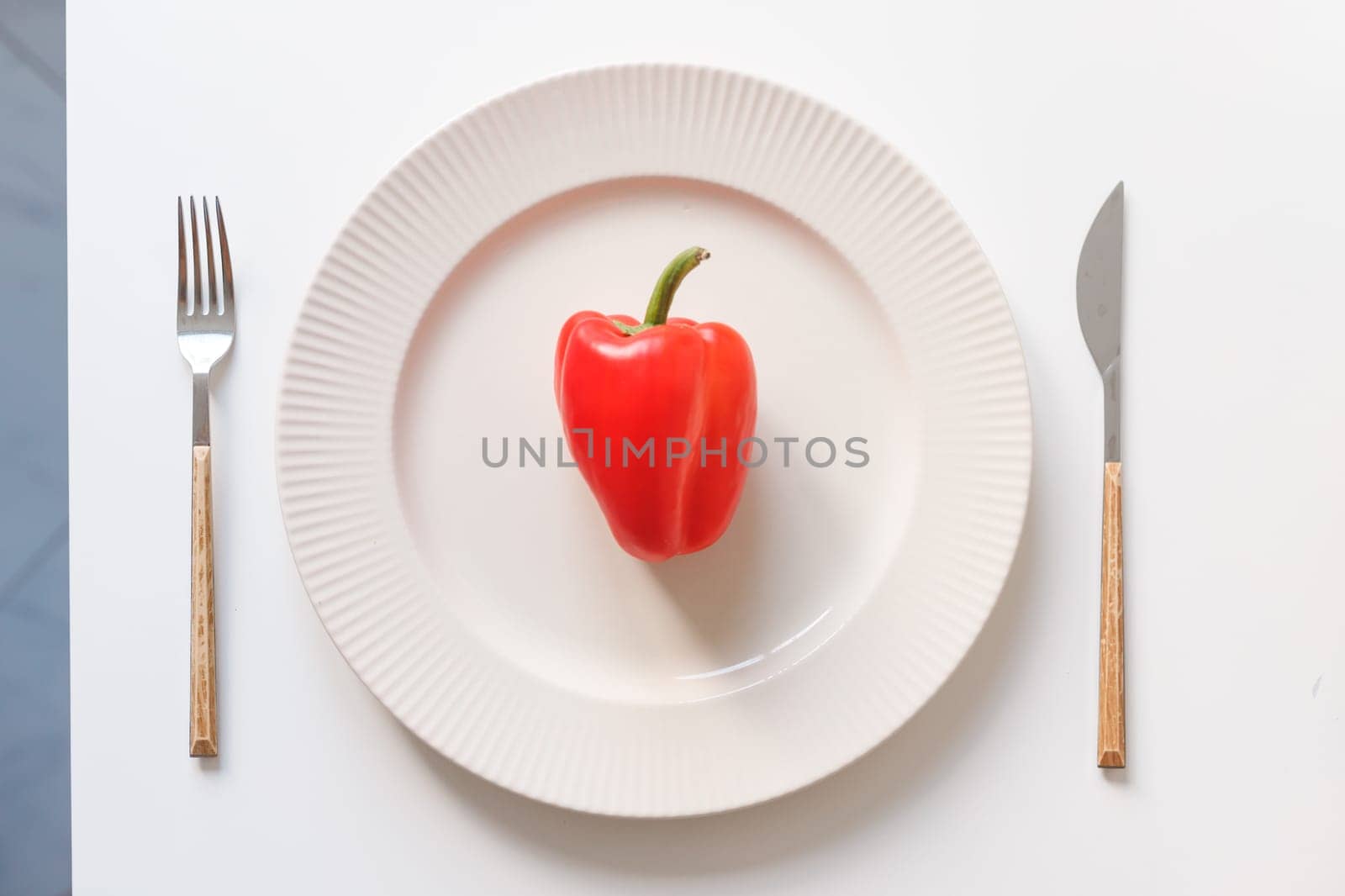 One red pepper in the dish. Fork and knife on white table. Vegan meal concept, diet concept.