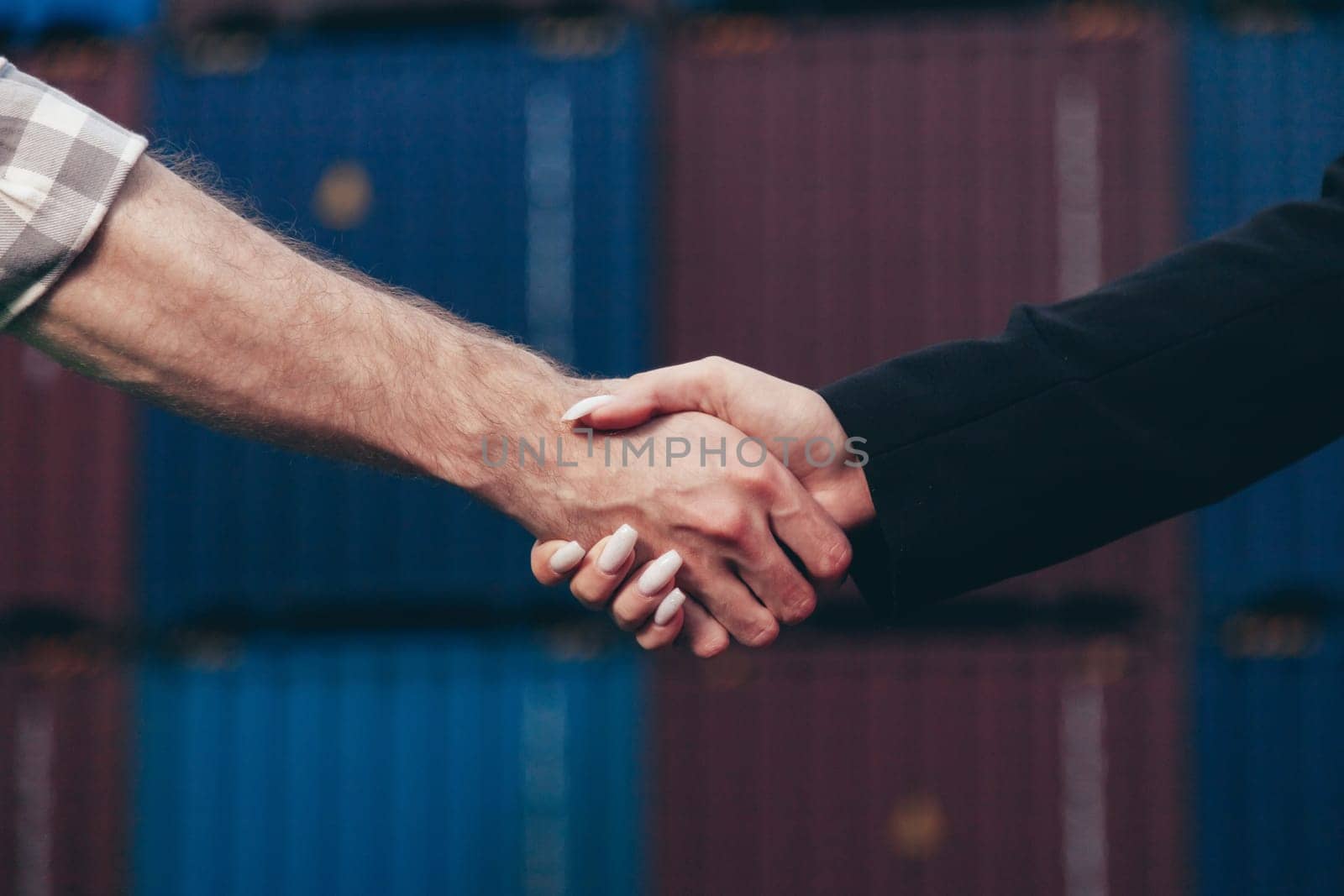 People at work: man and woman hand shaking at shipping terminal with containers in background.