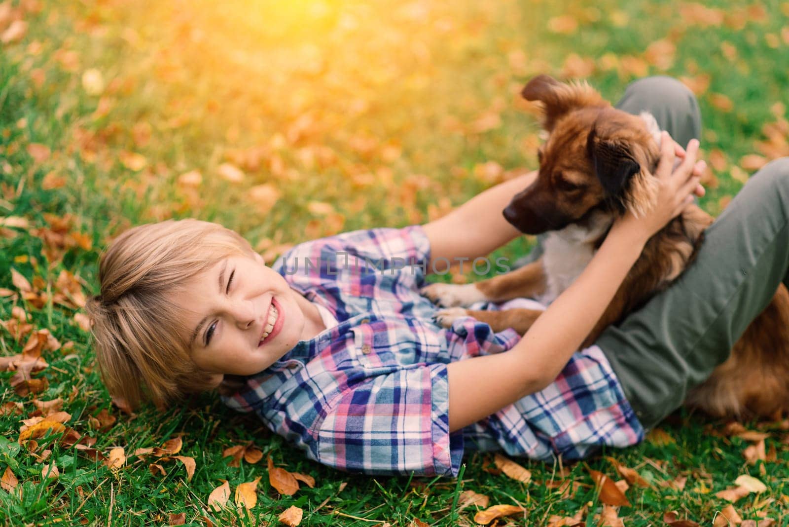 Boy hugging a dog and plyaing with in the fall, city park