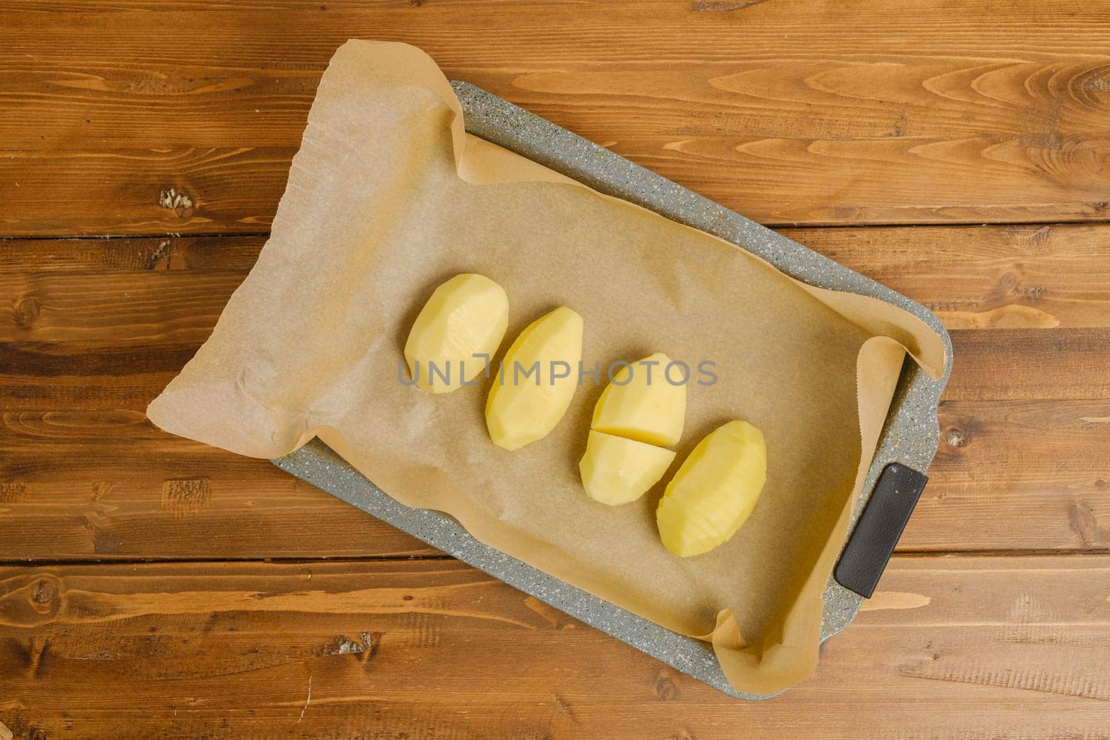 Top view of sliced hasselback potato on a parchment in baking tray