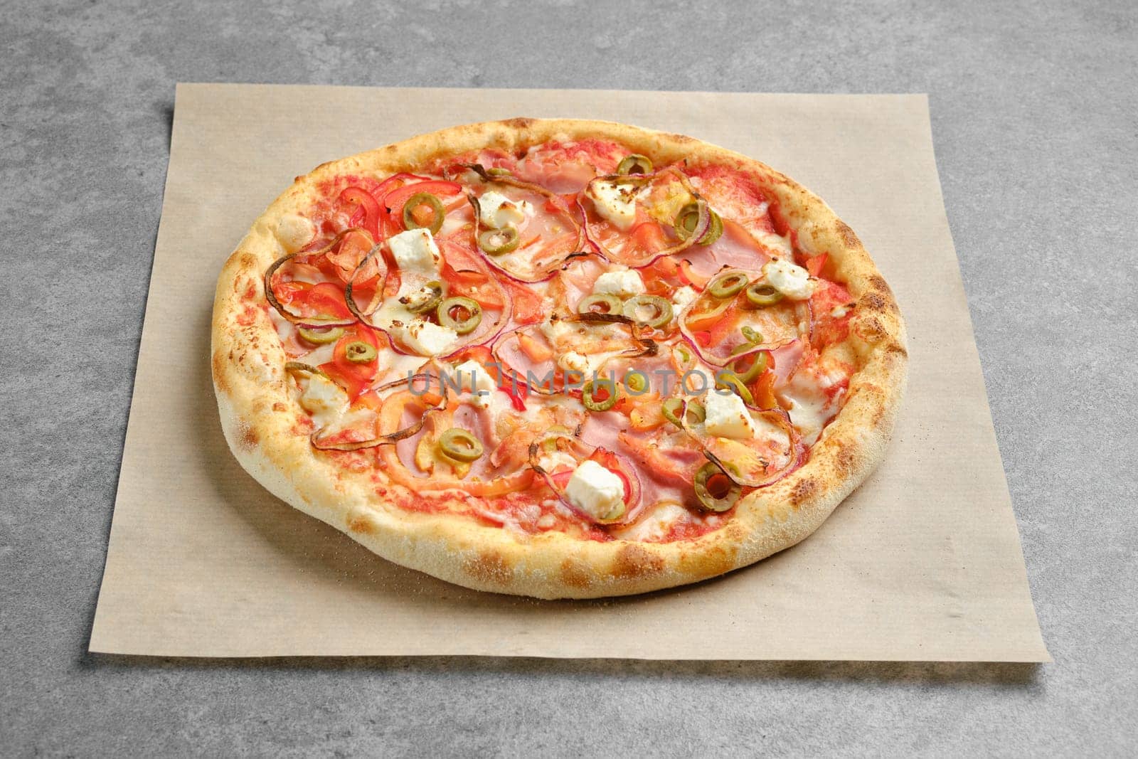 Top view of pizza with ham, onion and feta cheese on parchment paper