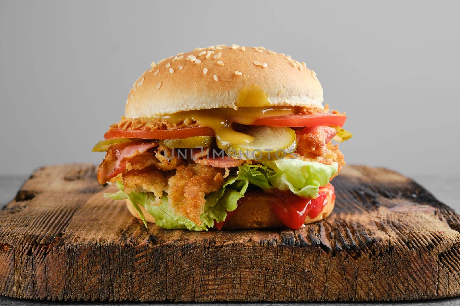 Kentucky chicken burger with pickled cucumber and fresh tomato on wooden background, front view