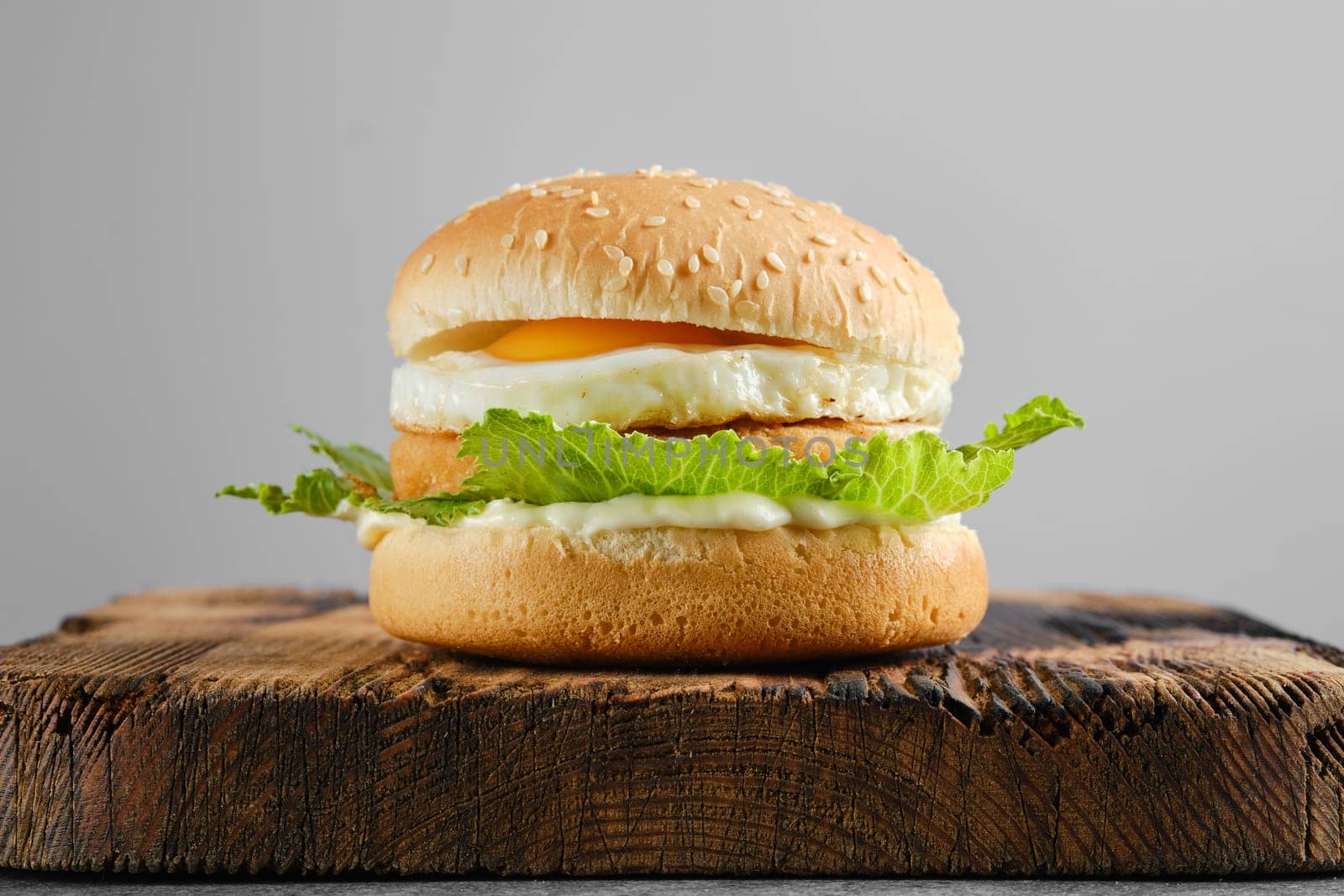 Chicken burger with fried egg and fresh iceberg lettuce salad on wooden board, front view