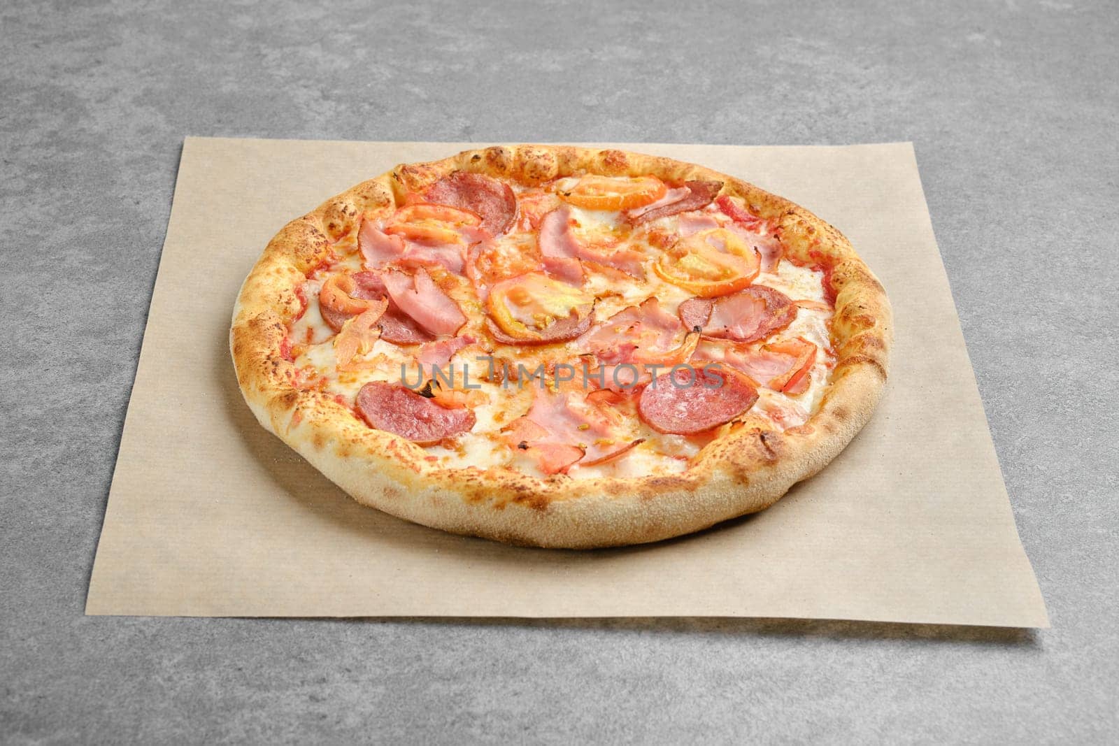 Pizza with ham, cured sausage and tomato slices ion parchment paper