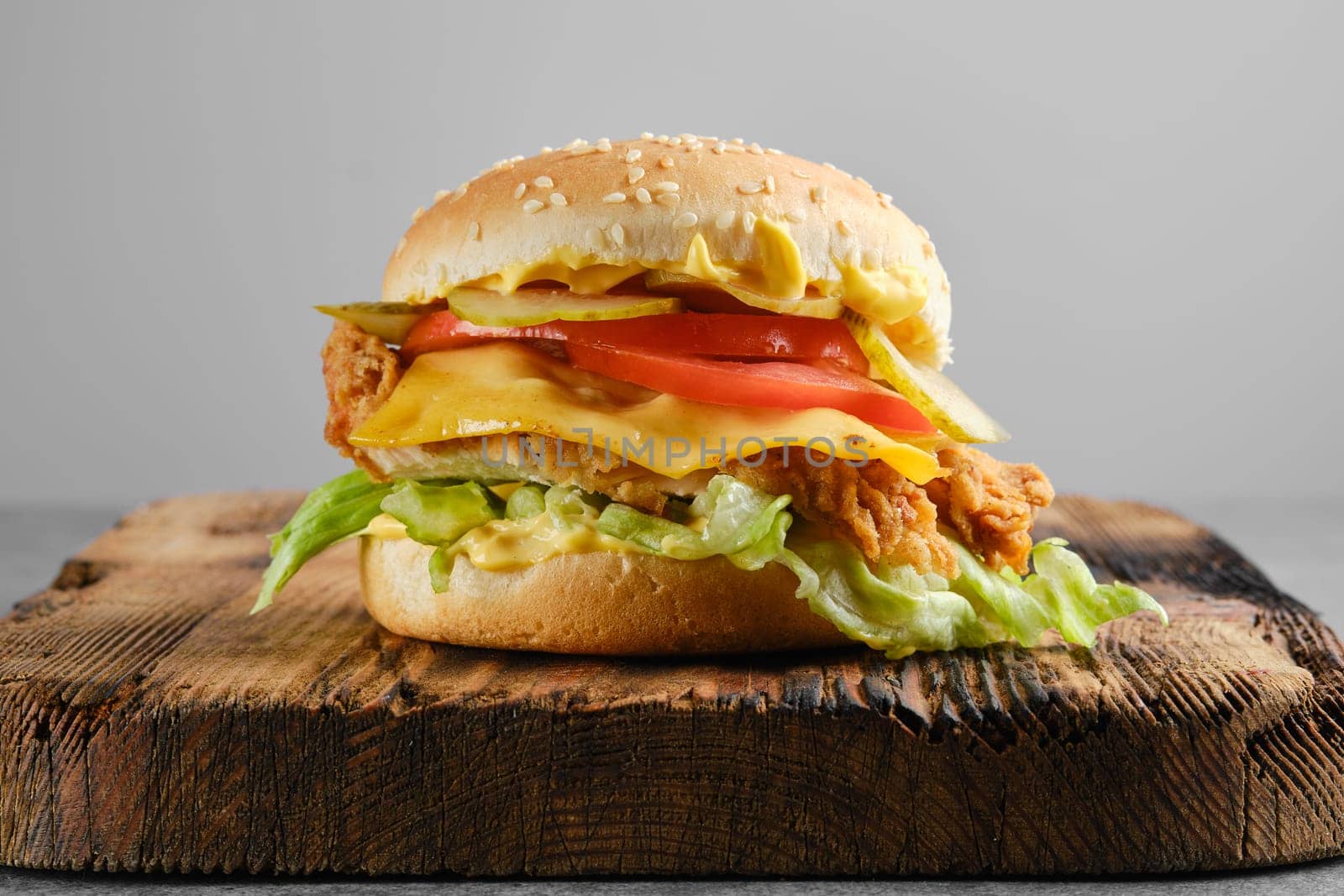 Chicken cheeseburger with fresh and pickled vegetables on wooden background, front view