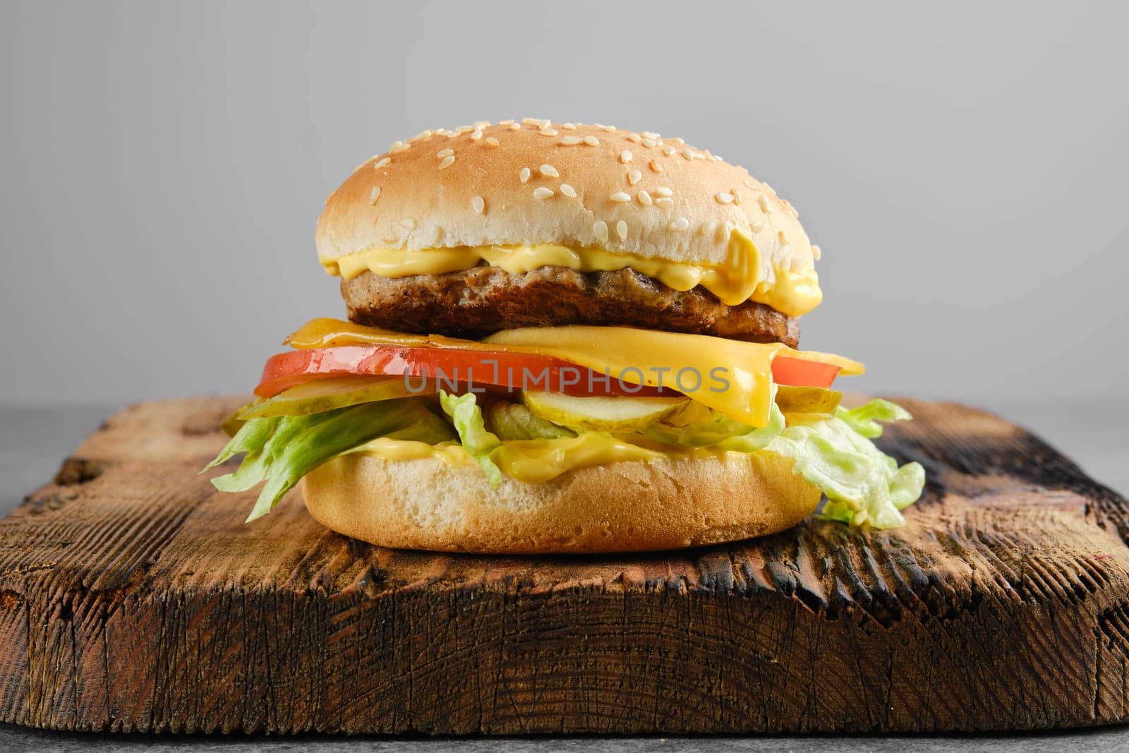 Beef cheeseburger with vegetables and cheesy sauce on wooden board, front view