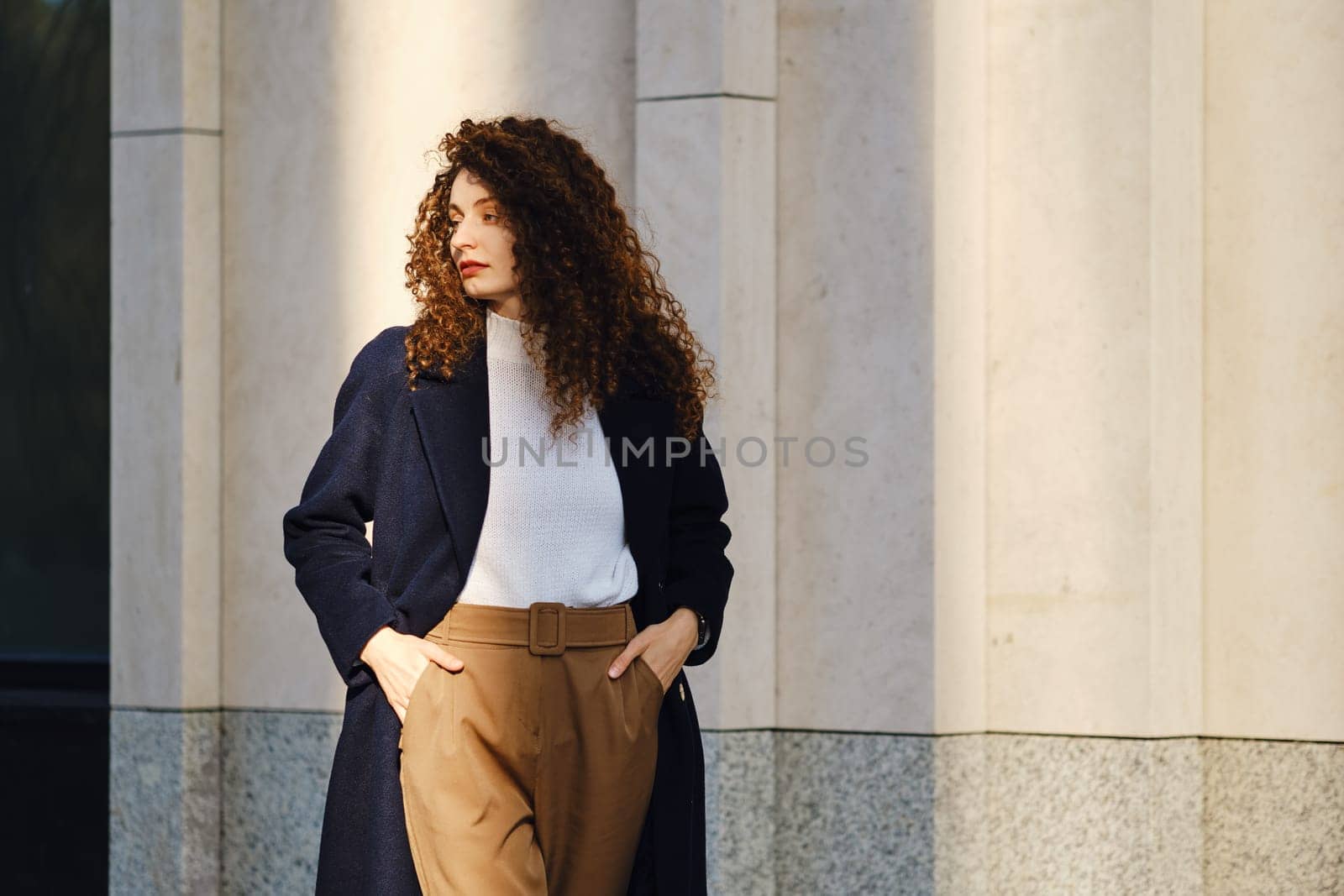 Young woman in wool coat and trousers posing on the street, looking to the side