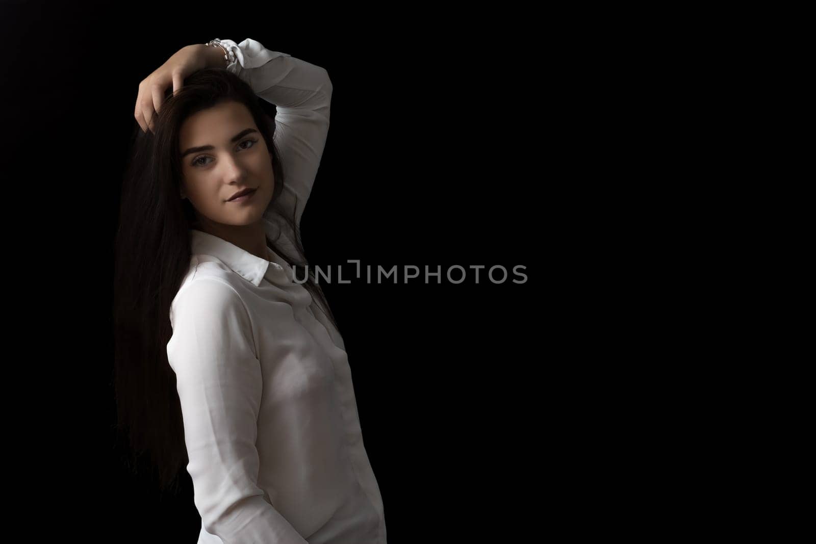 Smiling brunette girl is posing in studio on black background.  Horizontally.