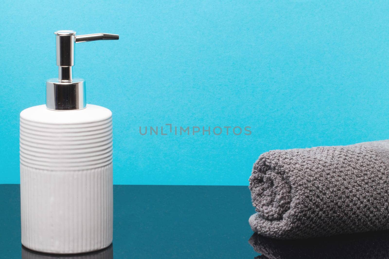 Macro of a beauty cosmetic makeup bottle and a fresh soft terry bath towel on dark table over blue background. Copy space for product display montage.