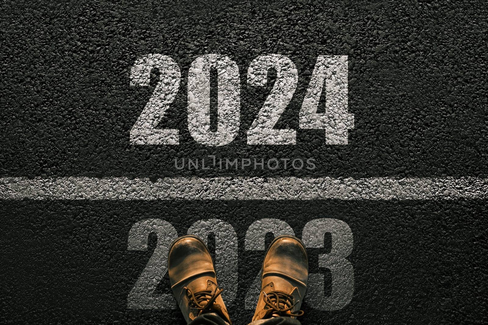 Man walks on asphalt and crosses the line by 2024. New year 2024. Men's legs with leather shoes go to 2024. End of 2023 and beginning of 2024