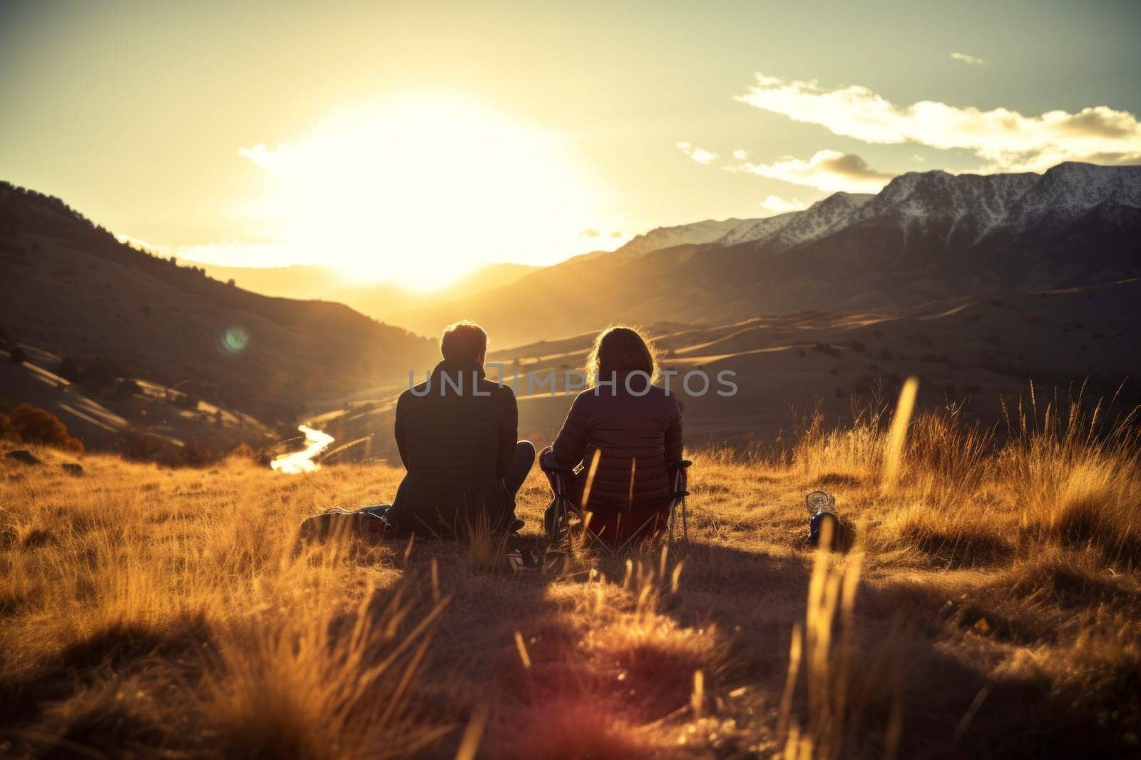 Couple sitting at campfire in evening during mountain trip. Couple having fun sitting at bonfire admiring mountain landscape. People relaxing at fire in the evening. Weekend trip. Travel to the mountains. Beauty in nature