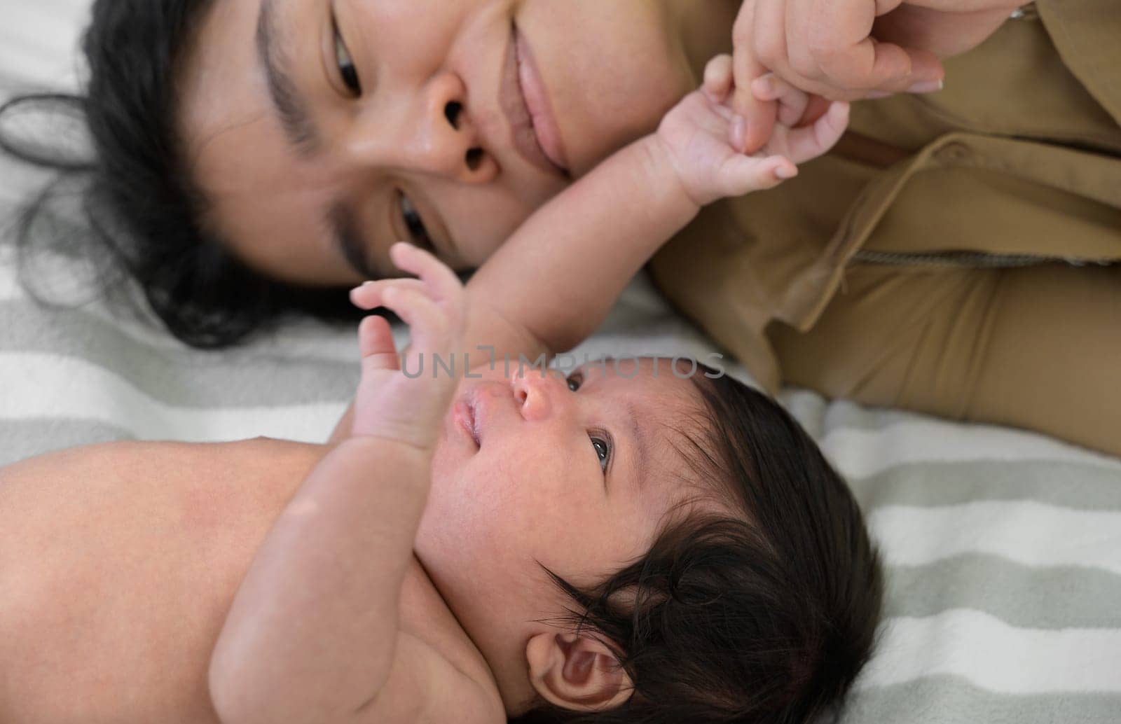 Mother and child on white bed. Mom and newborn baby girl in diaper playing and having fun together at home. Care, love and mothers day concept.