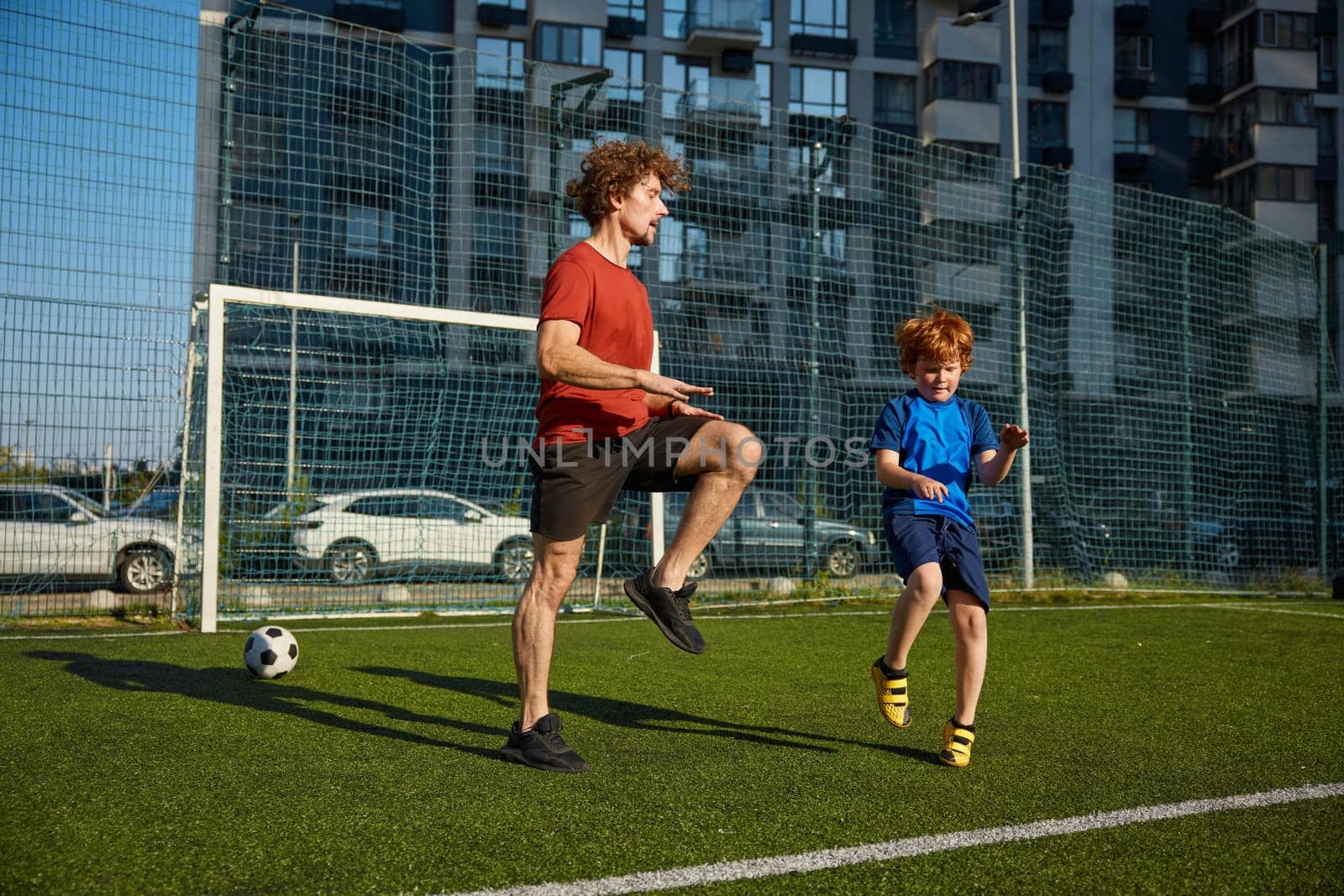 Sportive dad and son doing physical workout and warming legs up before football game training at city stadium