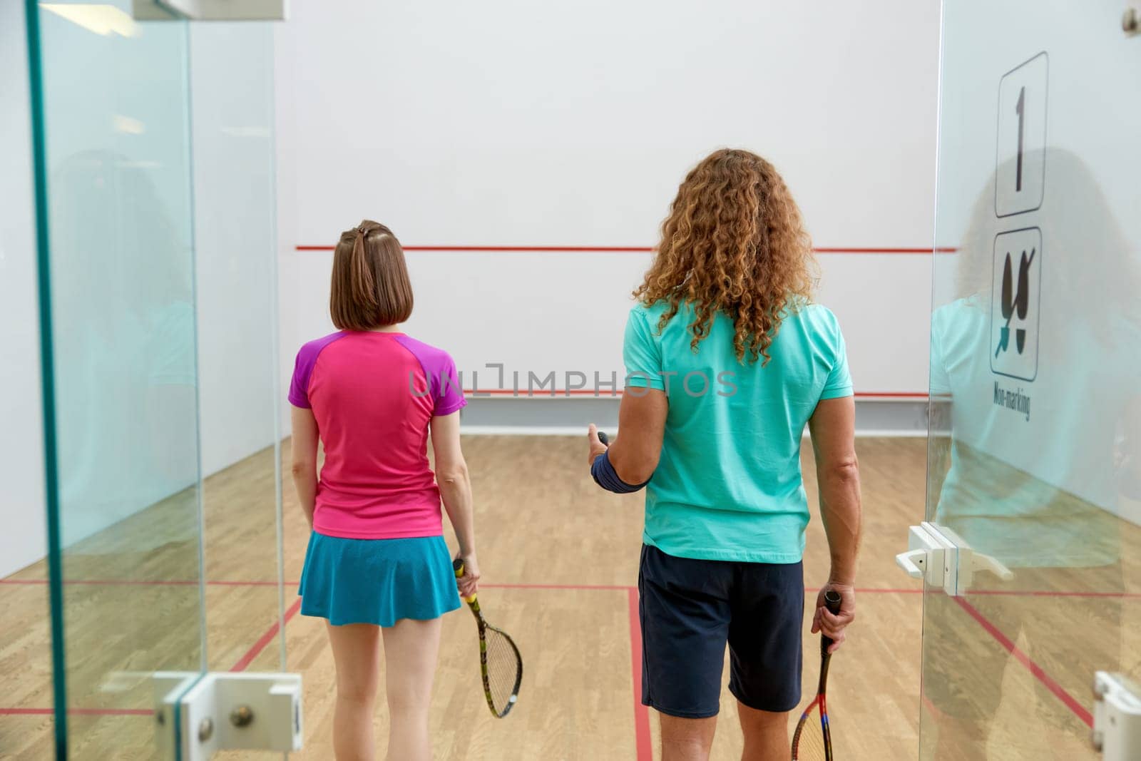 Man and woman squash player holding racket view from back standing in doorway of indoor sport court. Concept of healthy and active lifestyle