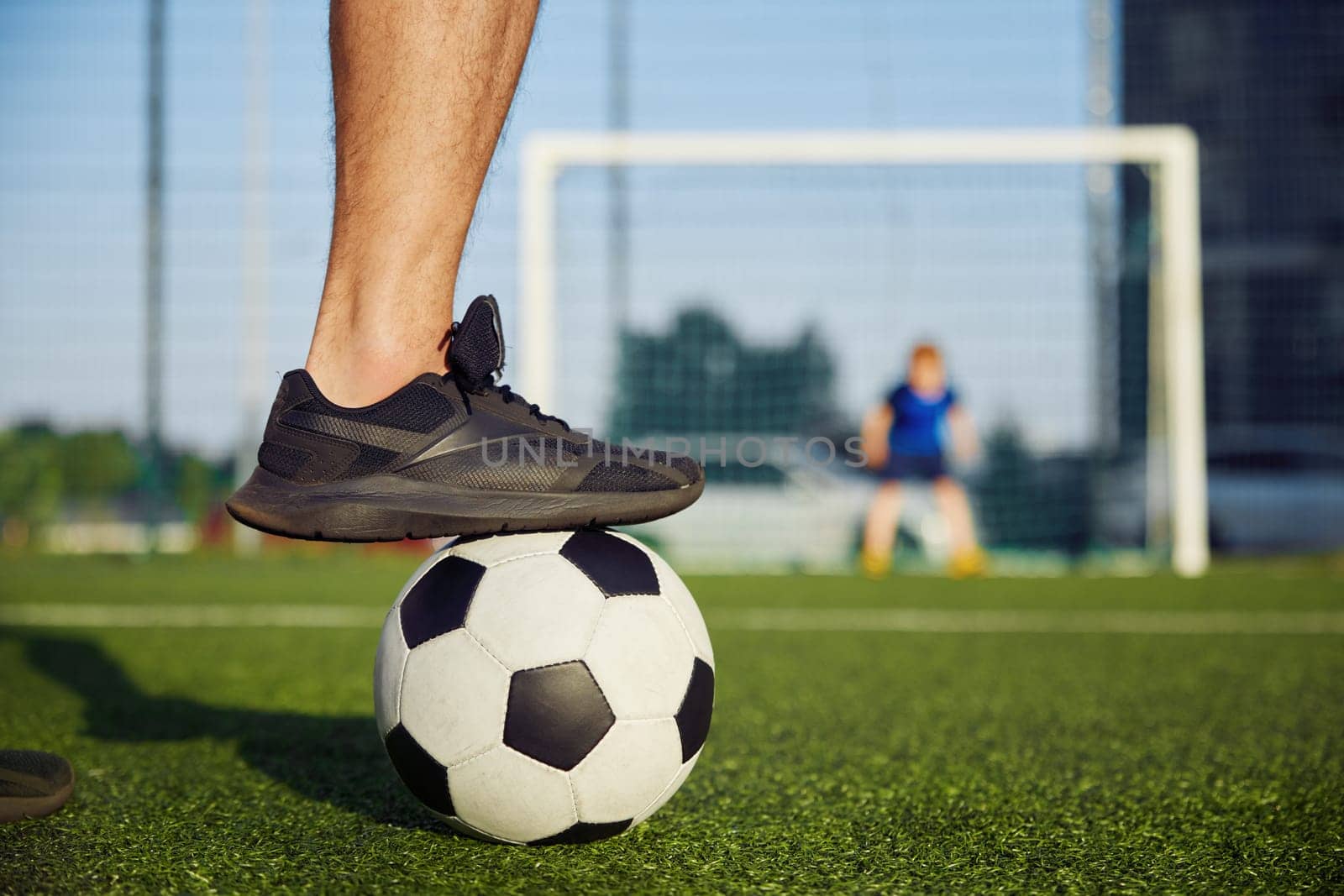 Happy family playing football on field. Focus on father foot on soccer ball. Dad preparing to hit goal, son defending gate