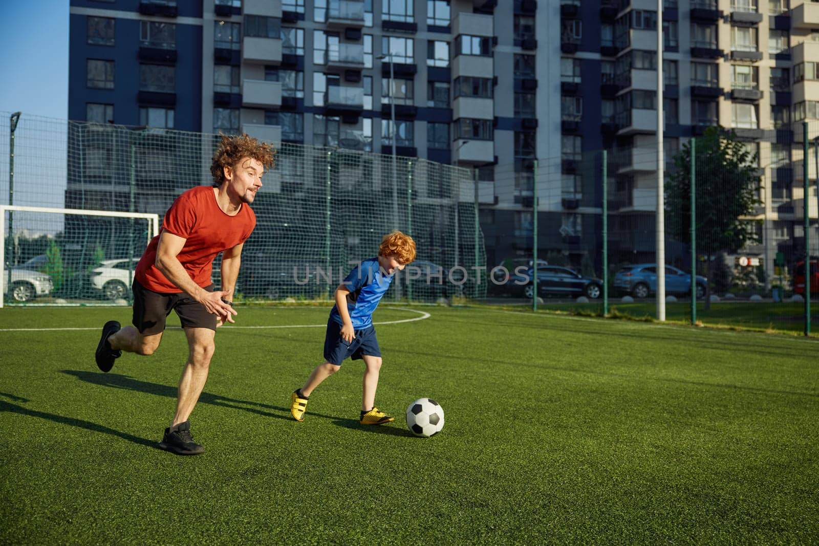 Dad and son child playing soccer on field. Friendly confrontation of parent and kid. Happy family playful time together