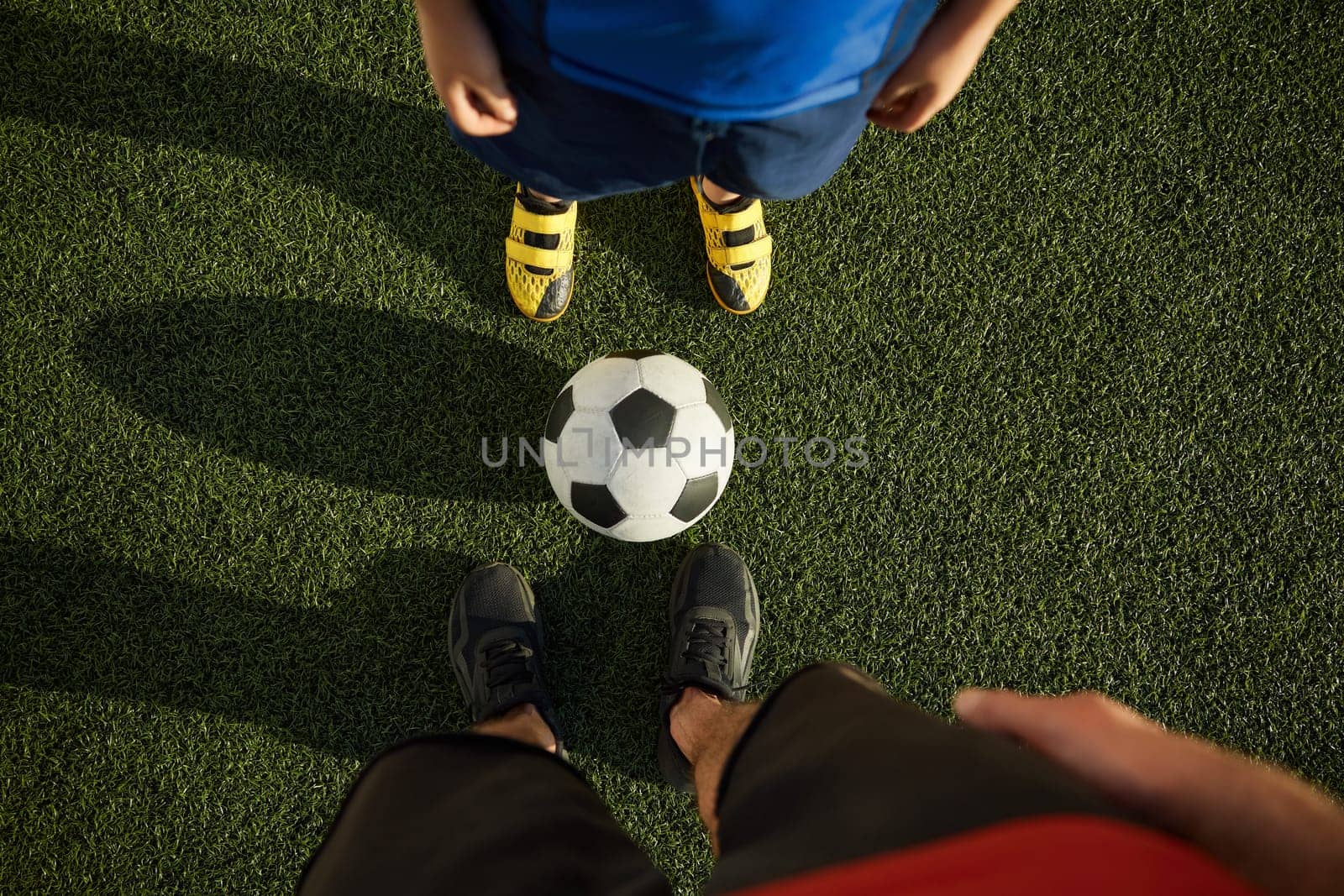 Father and son child playing football on outdoor field. Focus on feet of adult and young soccer players