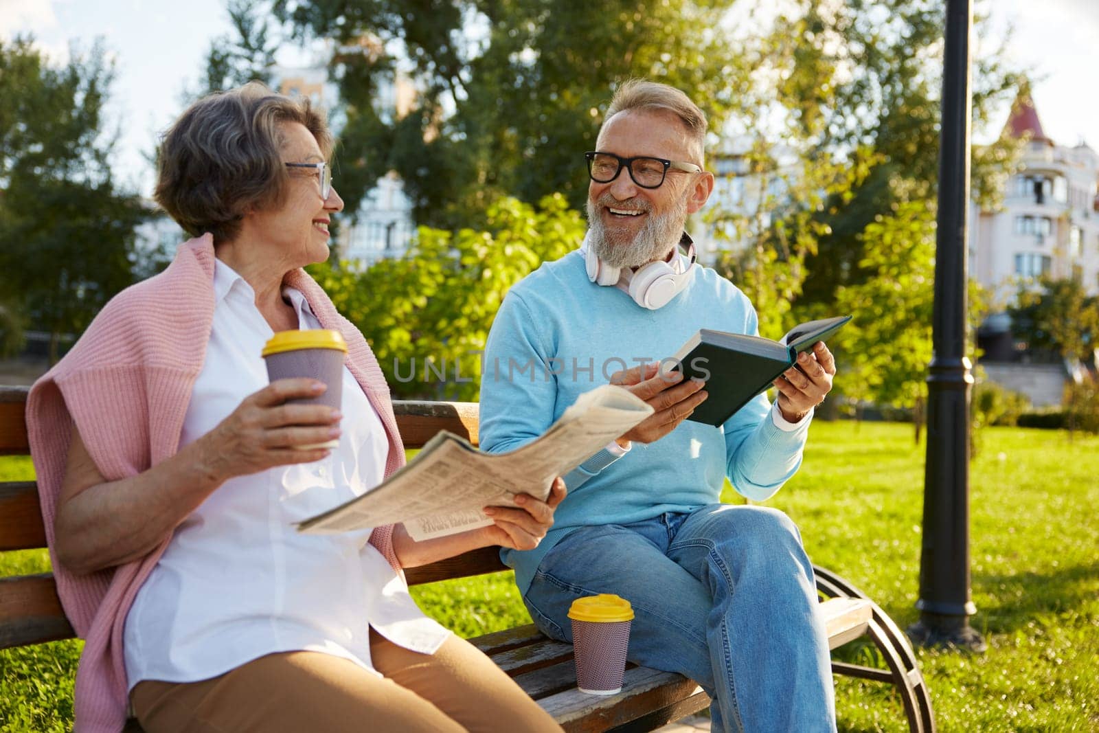 Concentrated man and woman couple reading on city park bench. Happy retirement and free weekend time