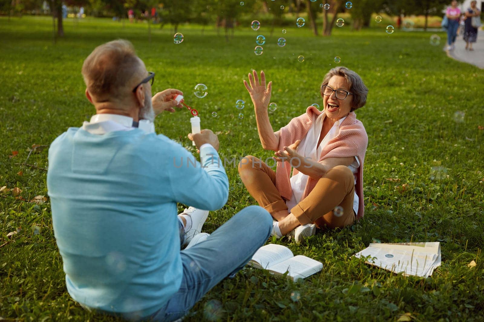 Playful active senior couple blowing soap bubbles while rest in city park. Vitality and active elderly people concept