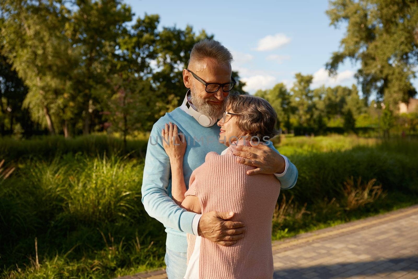 Smiling senior couple hugging with love feeling bonding and gratitude to life giving chance to be happy on retirement. Public green park city outdoors background
