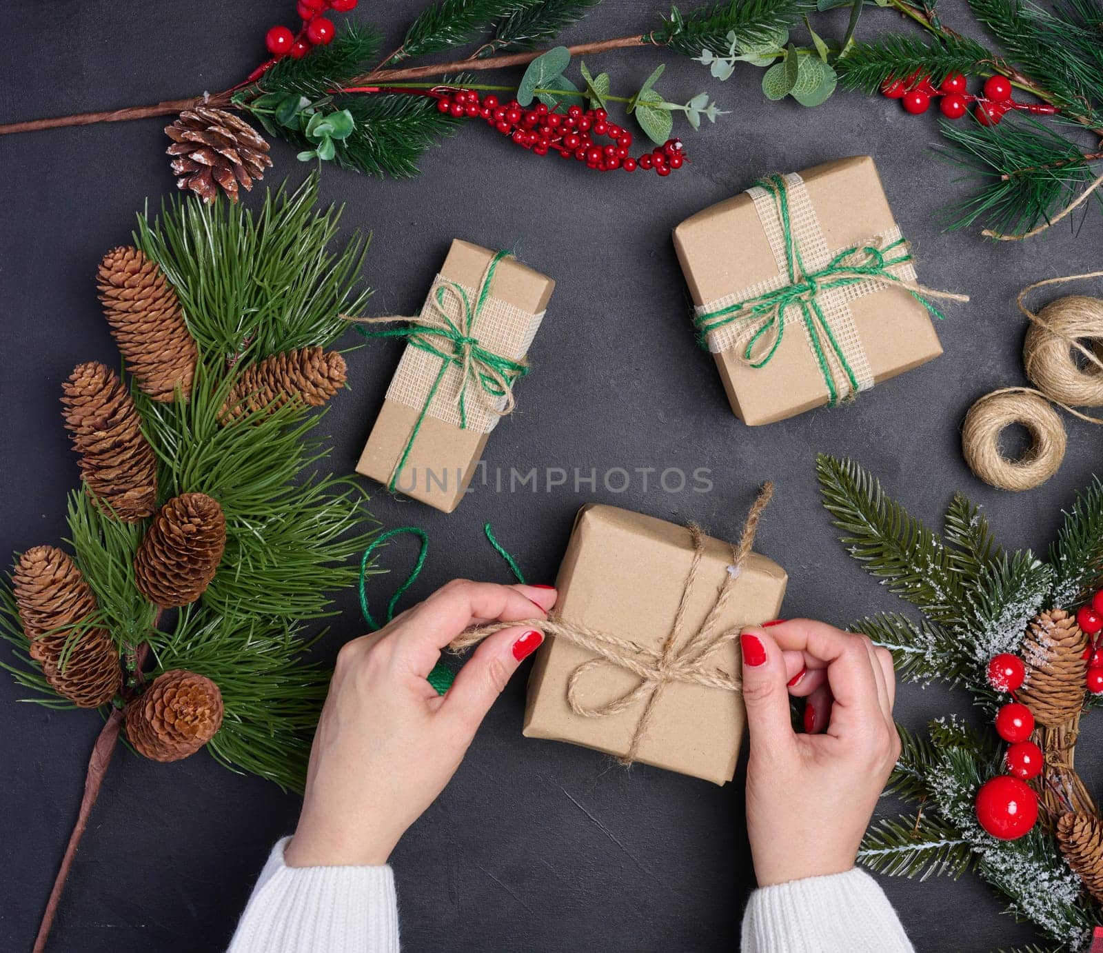 A woman is packing gifts, the pre-holiday bustle and preparations for Christmas. Gifts wrapped in brown paper and tied with green ropes are laid out on the table