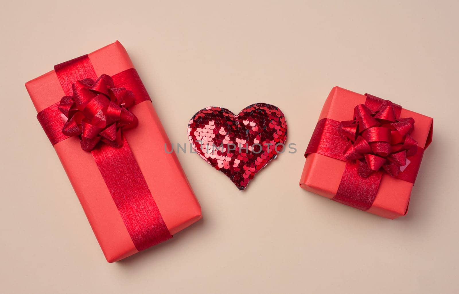 Red heart and boxes packed in red paper and tied with ribbon on a beige background, gifts
