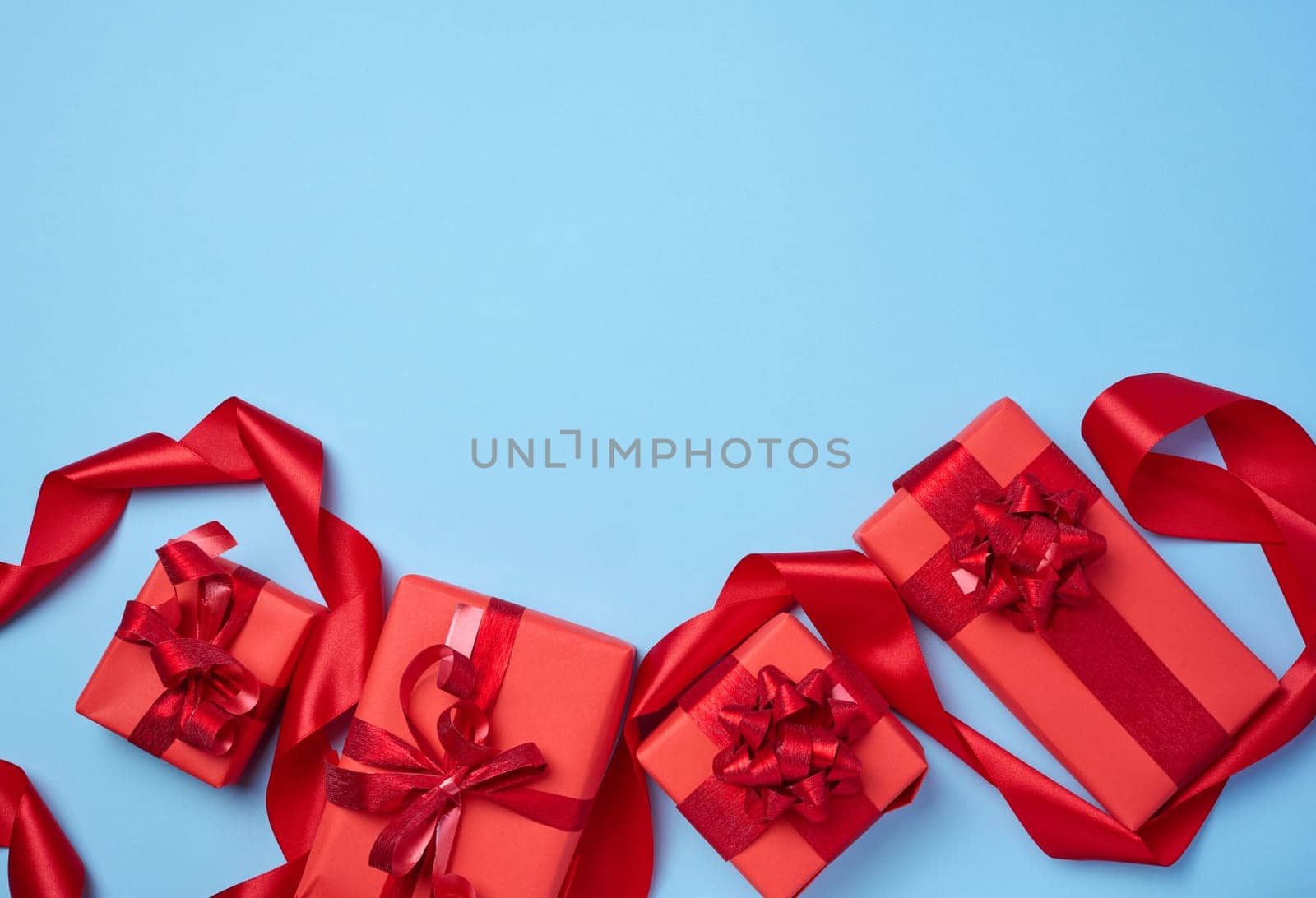 Boxes packed in red paper and tied with ribbon on a blue background, gifts. Copy space