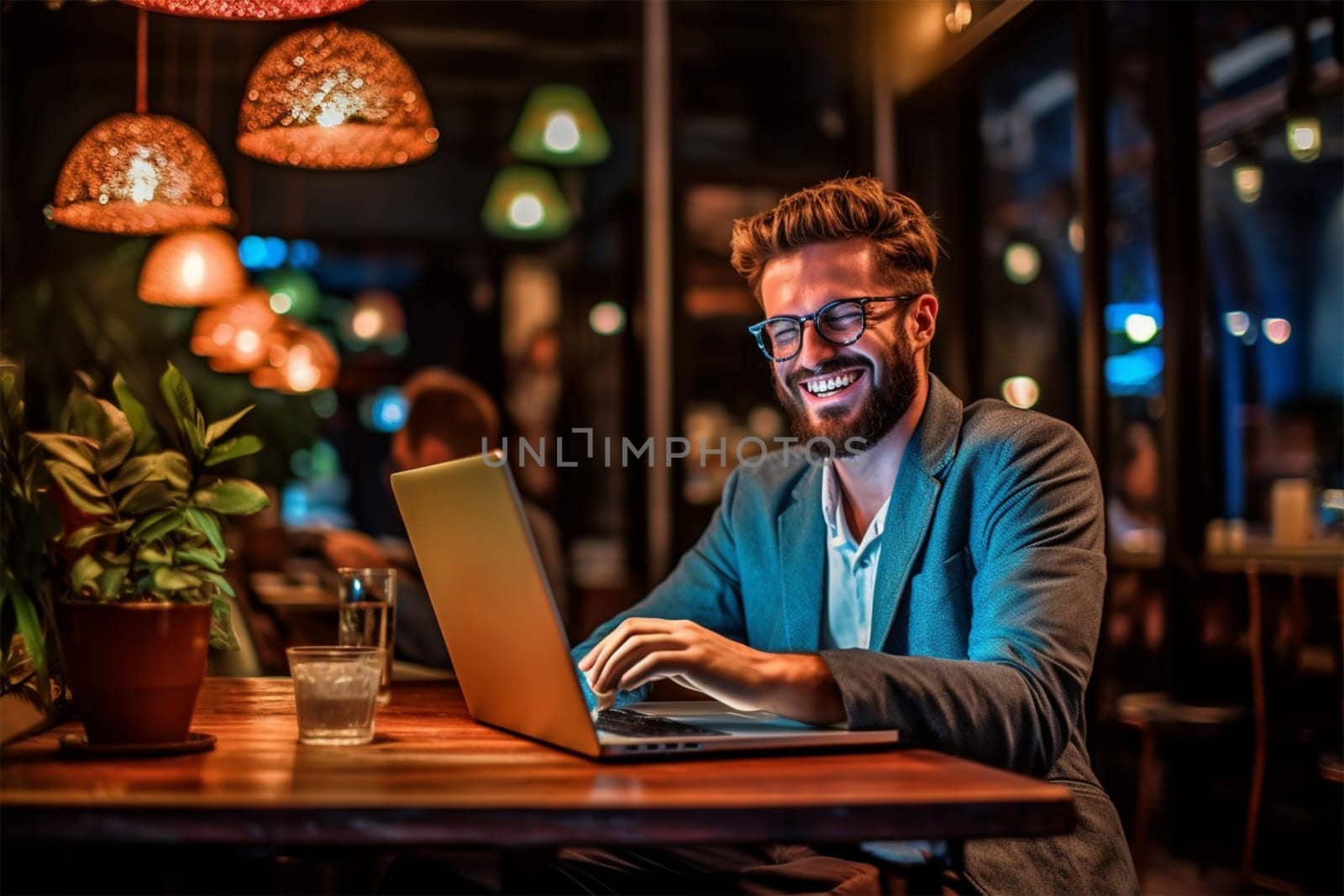 A young man works at a laptop in a cafe and smiles.