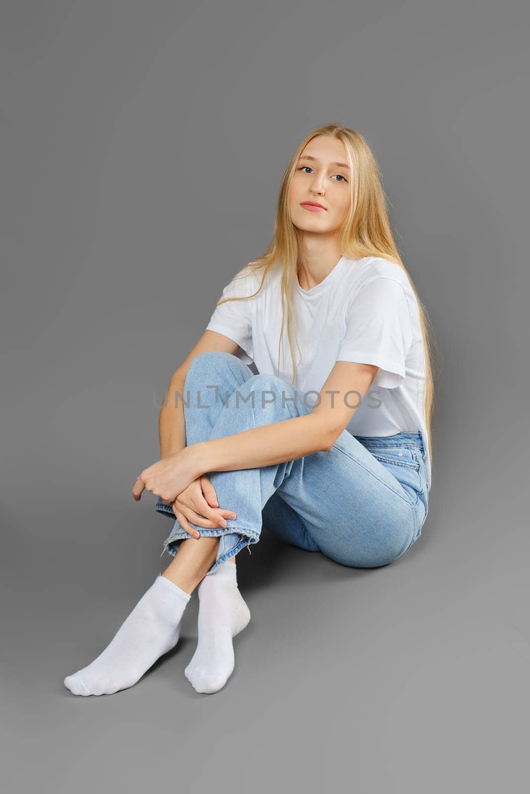 Thoughtful and calm woman sitting on the floor cross-legged on grey background