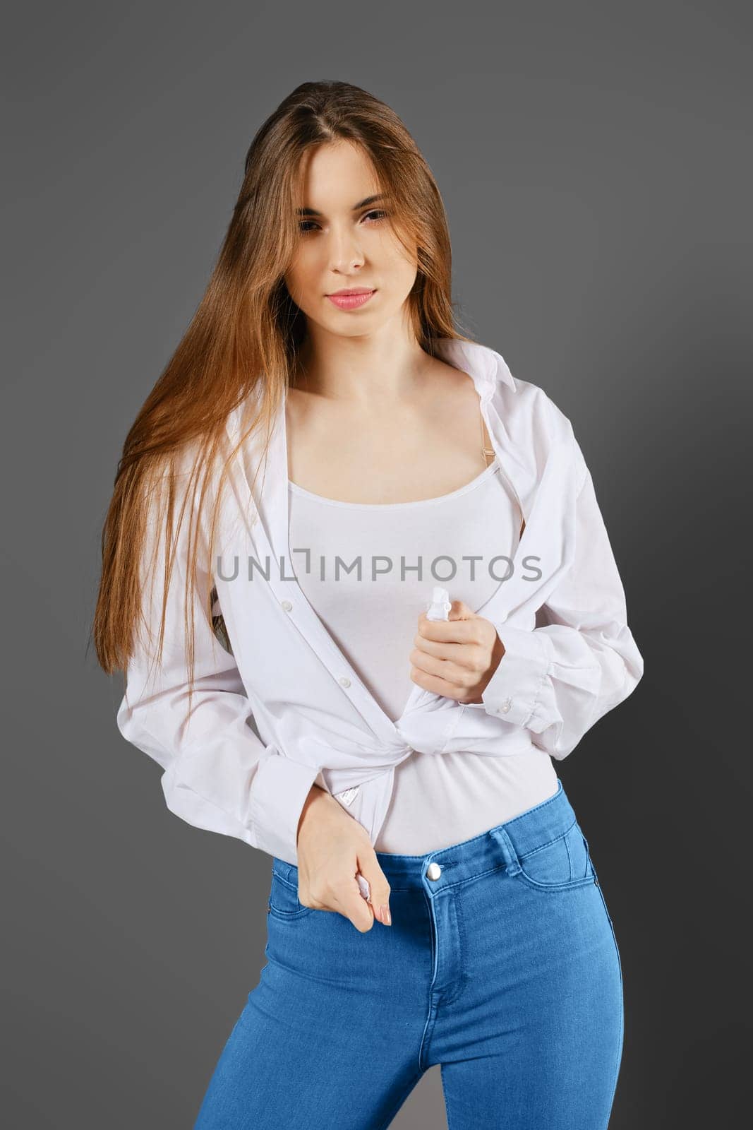 Young playful woman tying a shirt standing in studio on grey background