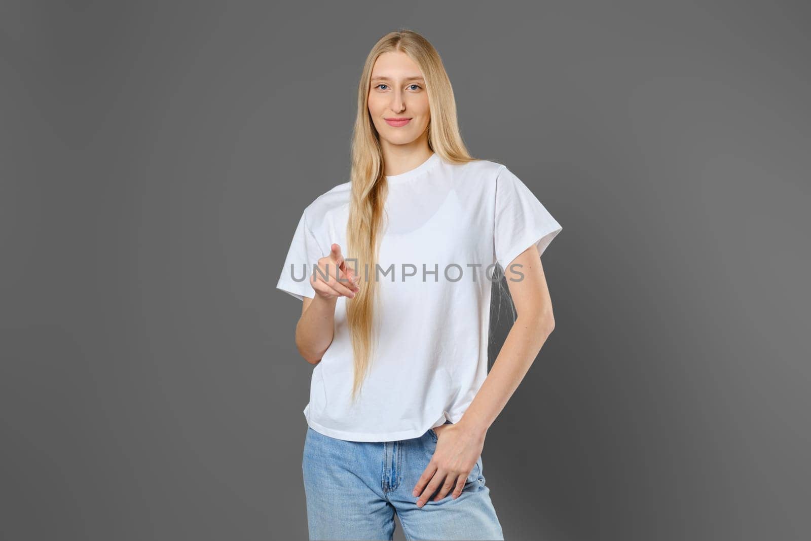 Cheerful blonde woman wearing jeans and shirt pointing forward with index finger