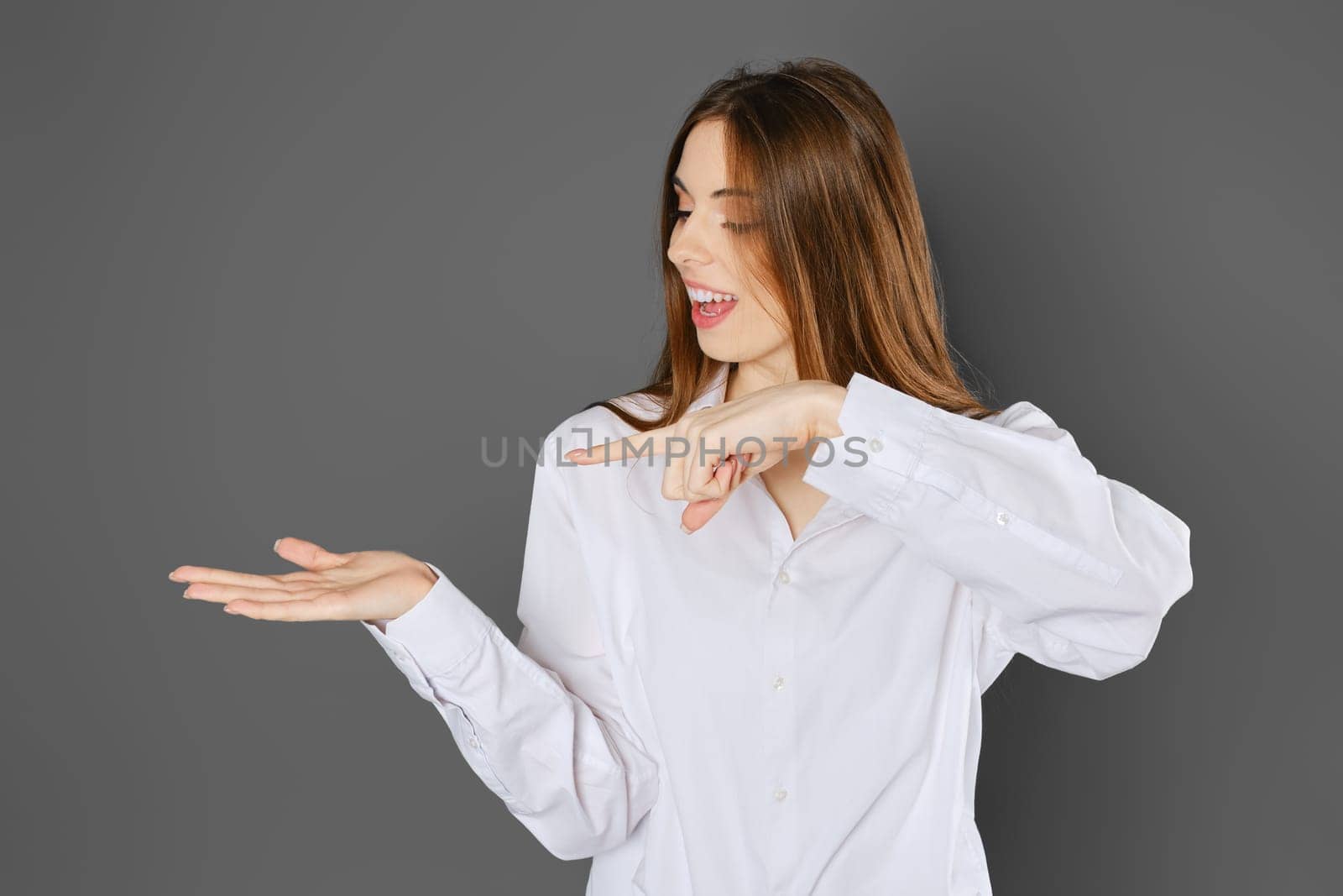 Exited young woman wearing white shirt pointing to her palm with index finger
