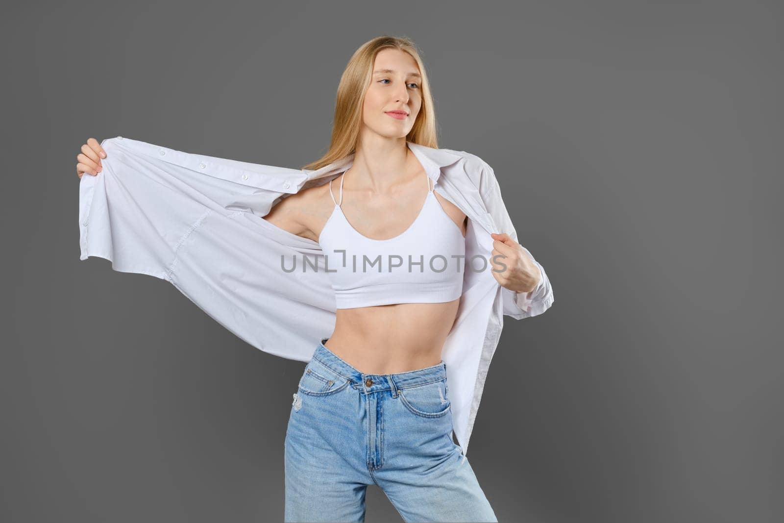 Young blonde woman putting on a shirt over a tank top