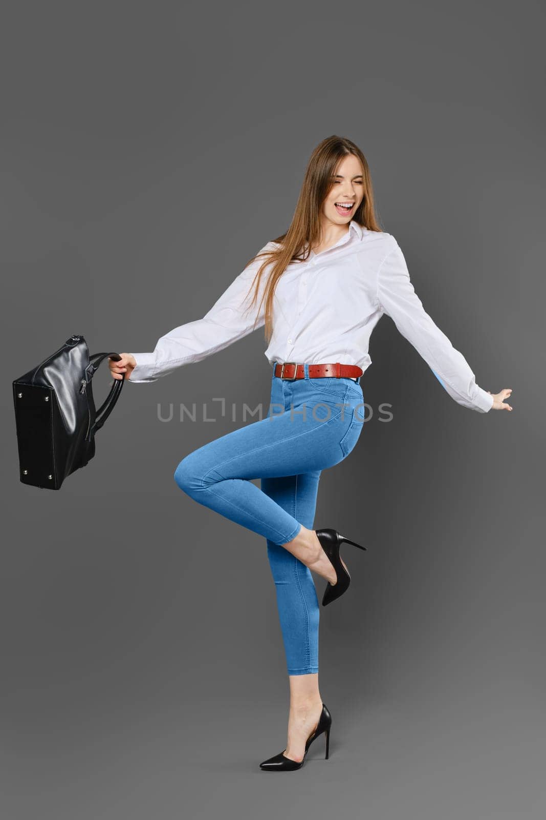 Joyful woman waving her arms while holding a bag and standing on one leg