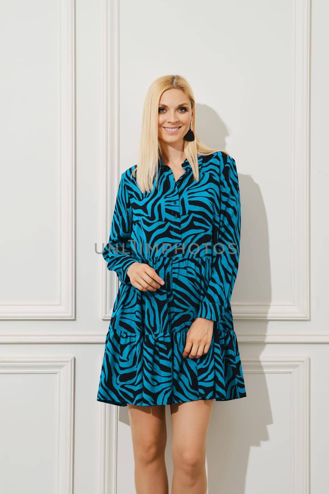 Smiling woman in short loose patterned dress standing by bright white wall