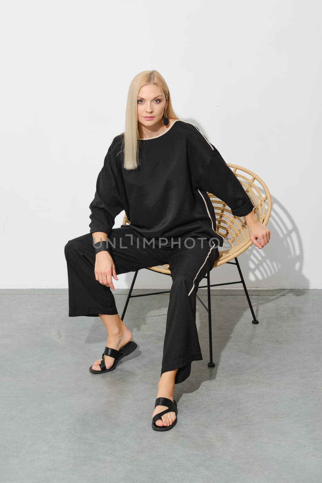 Portrait of blonde woman in loose casual clothes and leather sandals on a wicker chair