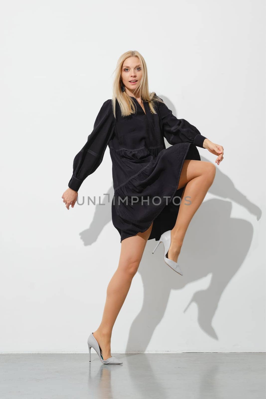 Blonde woman in a short loose dress takes a wide step with her leg raised high