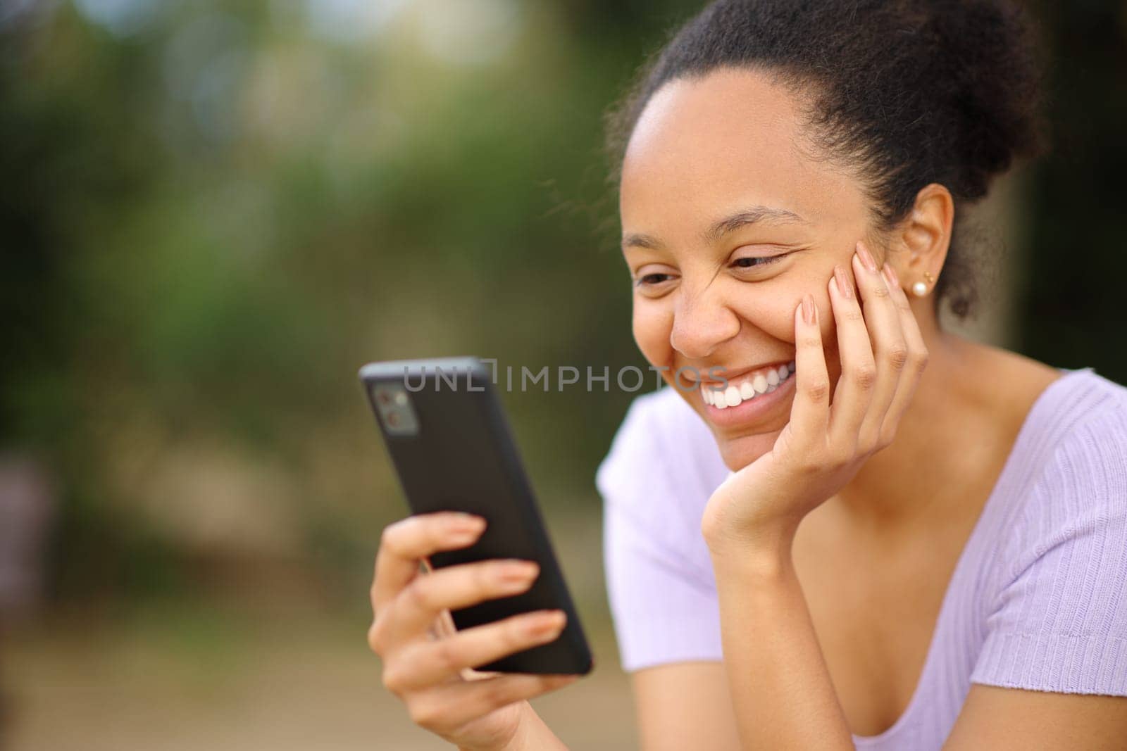 Happy black woman reading message on phone in a park
