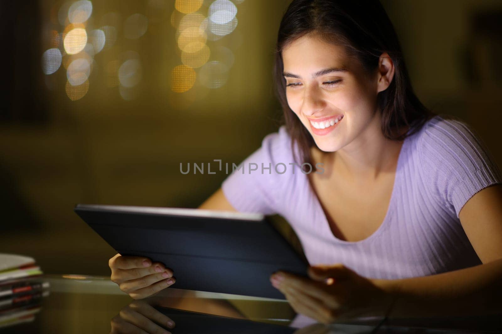 Happy woman watching media on tablet at night at home