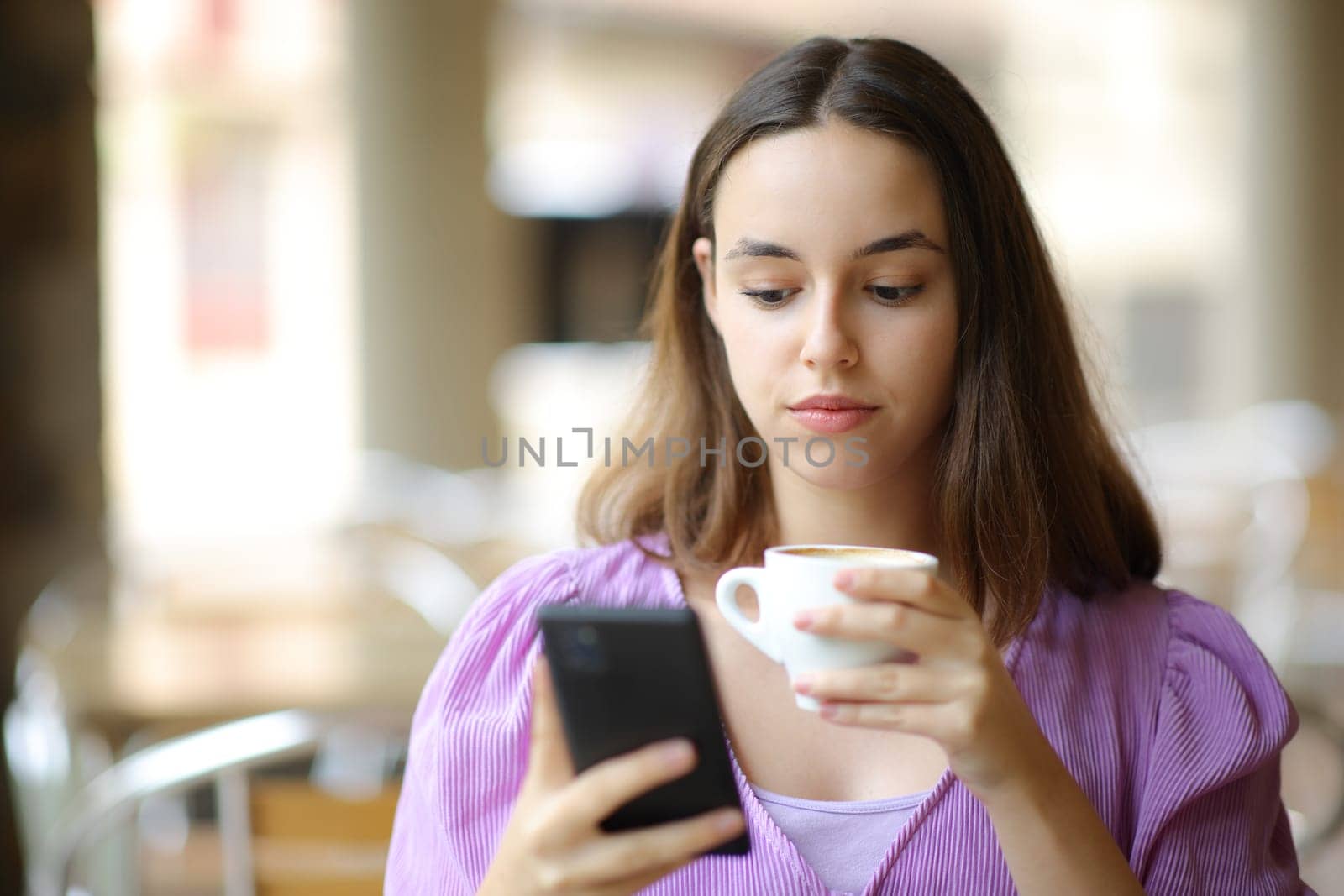 Front view portrait of a serious woman checking phone drinking in a bar terrace