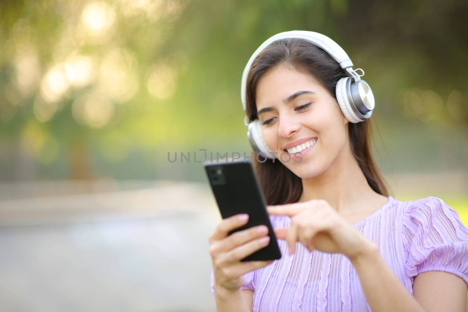 Happy woman listening to music using headphone and smart phone in a park