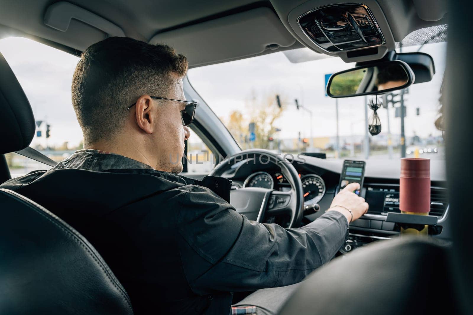 A man uses a smartphone installed in the holder while driving a car.