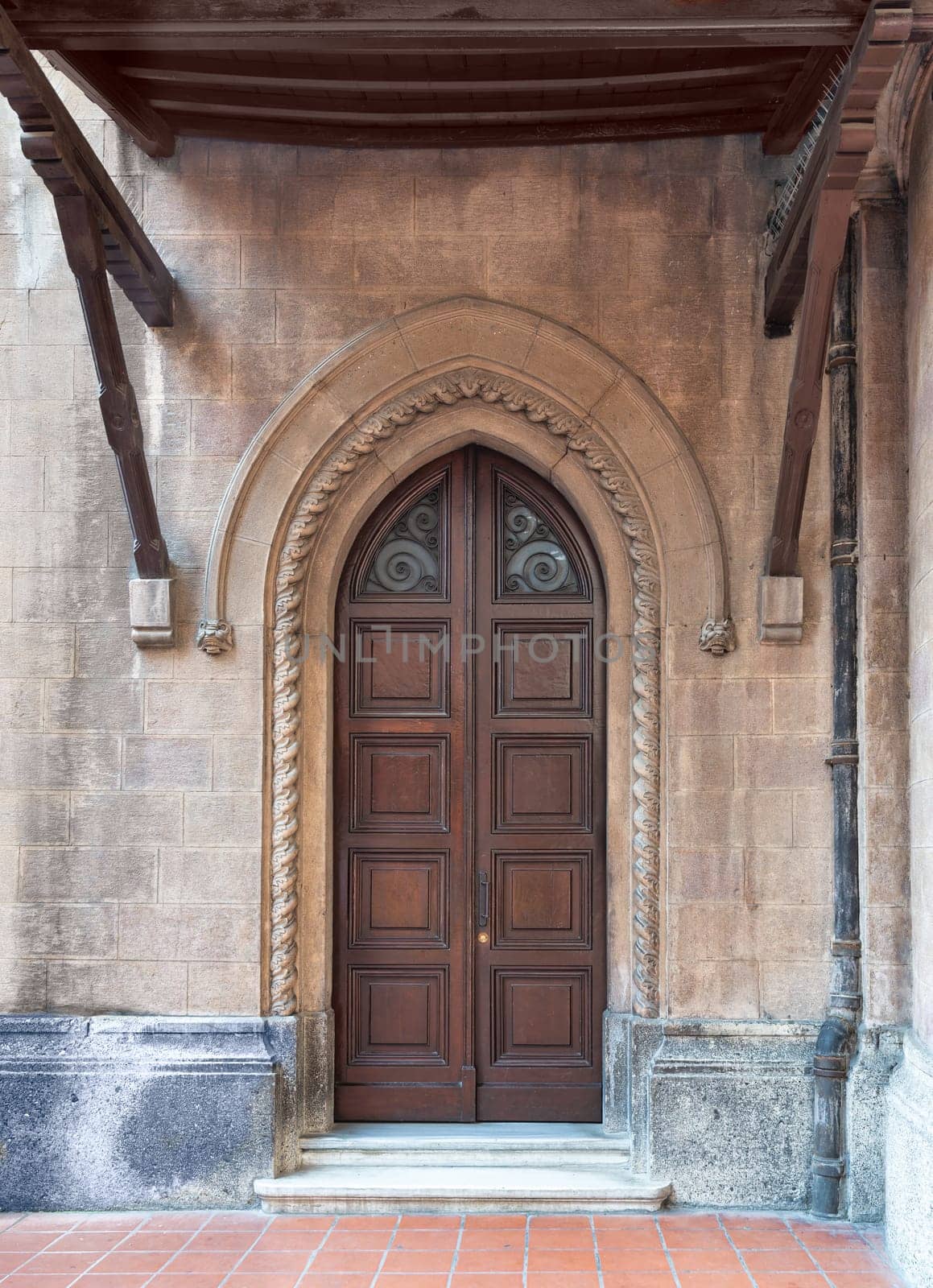 Close-up of a weathered wooden door in a brick wall. The door has a metal handle and a stained glass window in the upper part. The brick wall has a few cracks