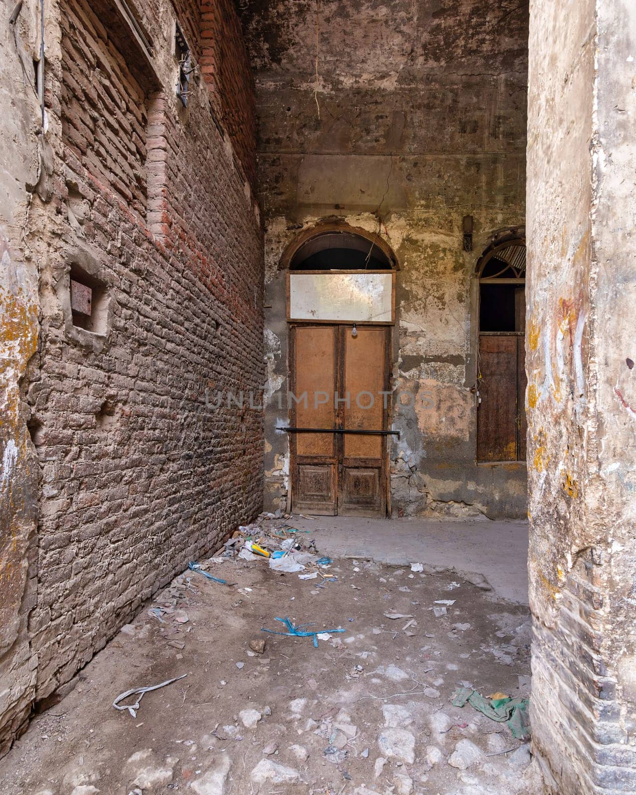 Narrow abandoned alleyway with old ruined side brick wall and old broken worn closed wooden door in the end