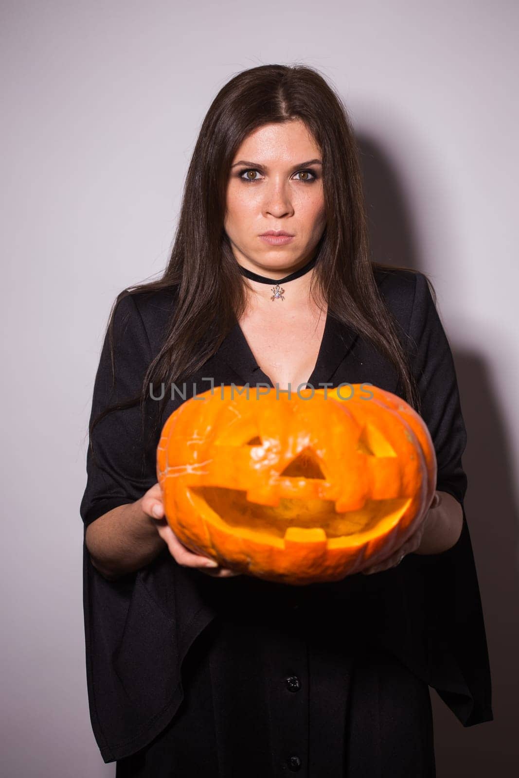 Woman as witch is standing with the pumpkin in the studio. Halloween and carnival concept.
