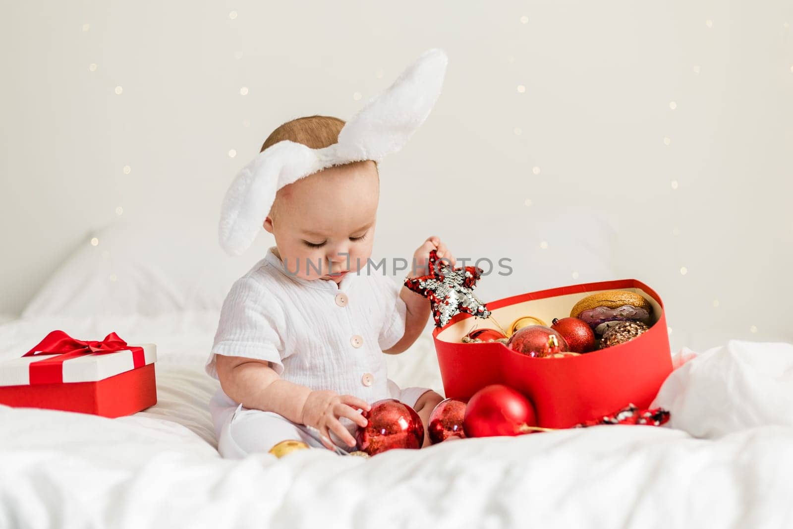 Christmas Baby in Santa Hat Child playing with baubles. Present Gift Box over Holiday Lights background and Merry Christmas