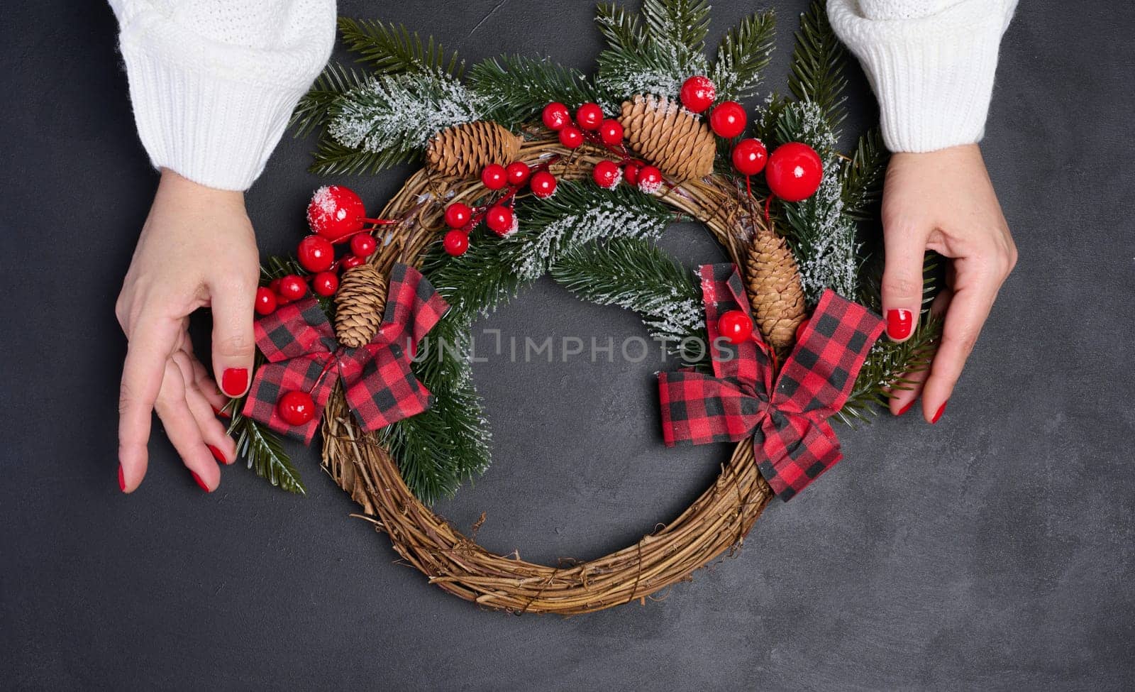 Two female hands holding a Christmas wreath on a black background, top view