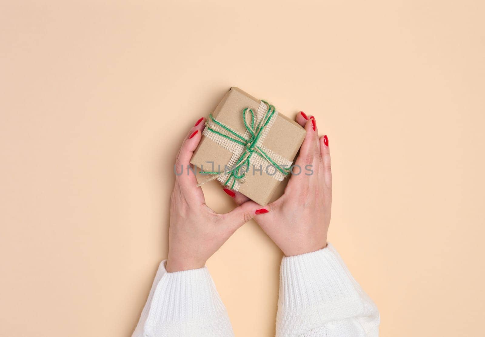 Female hands holding a gift box on a beige background. View from above