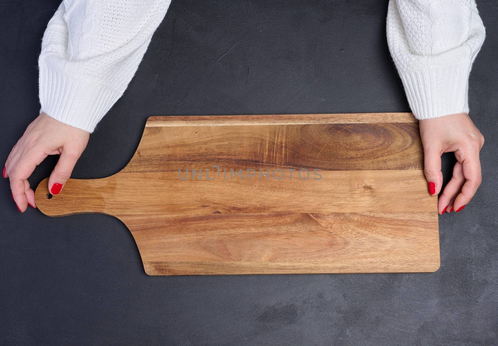 Empty wooden cutting board in female hands on black wooden table, top view
